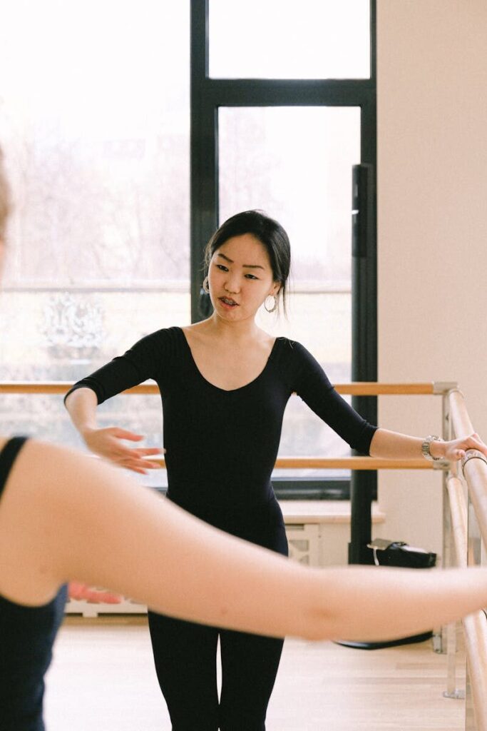 An instructor teaches ballet in a brightly lit studio, focusing on technique and form.